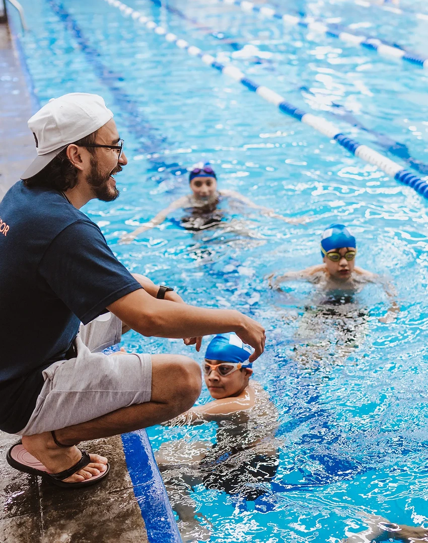 children in the swimming pool, man men in shorts sitting on side of pool wearing cap smile on face captured from side children in the swimming pool, man men in shorts sitting on side of pool wearing cap smile on face captured from side