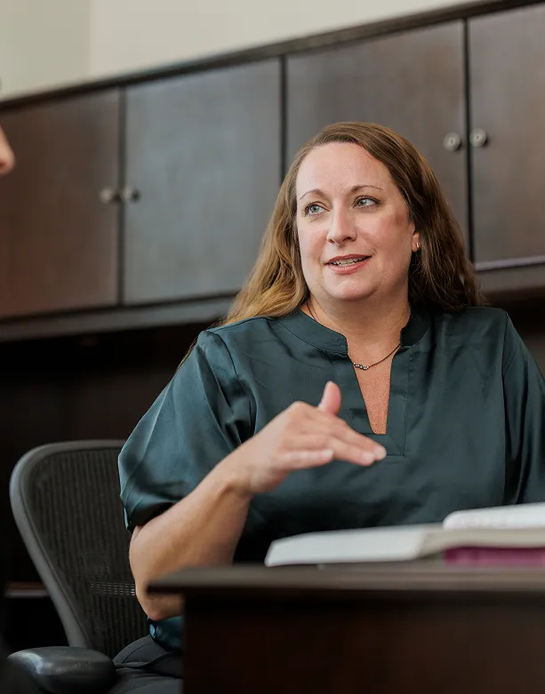 Two women conversing in a casual office setting, one seated and smiling Two women conversing in a casual office setting, one seated and smiling