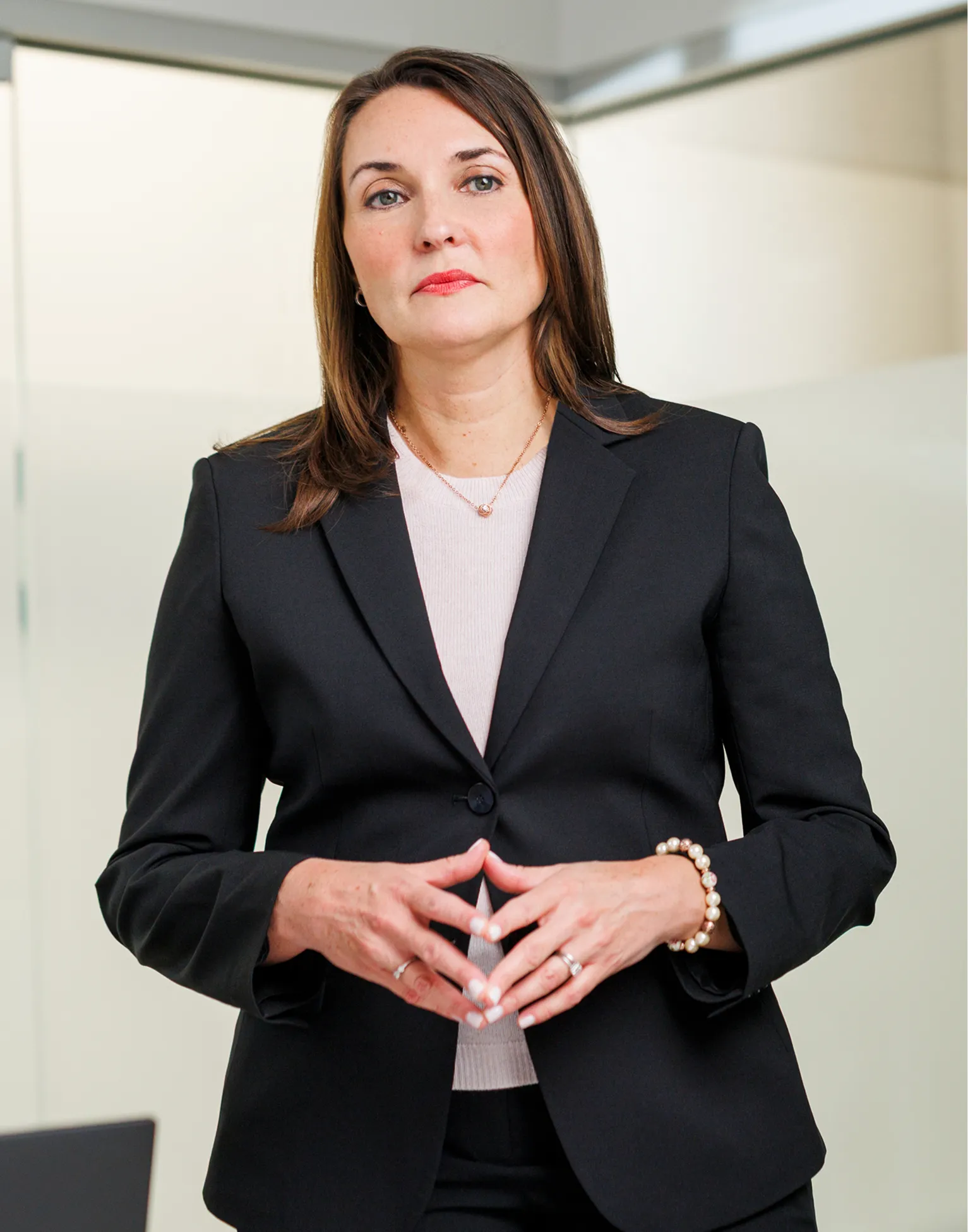 female in black suit standing and cross fingers face to camera listeining to someone not visible